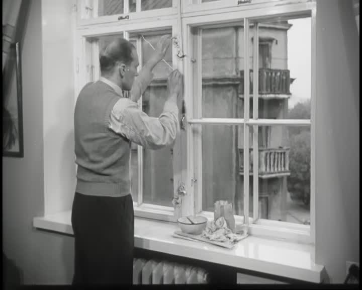Black-and-white image of a person sealing the edges of a window with a strip of paper as part of an energy-saving demonstration.